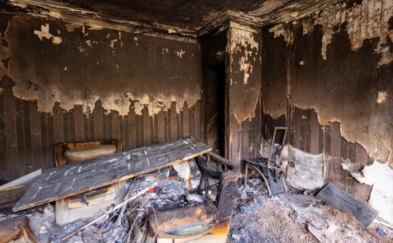 Fire-damaged room with charred walls, ceiling, and debris before restoration